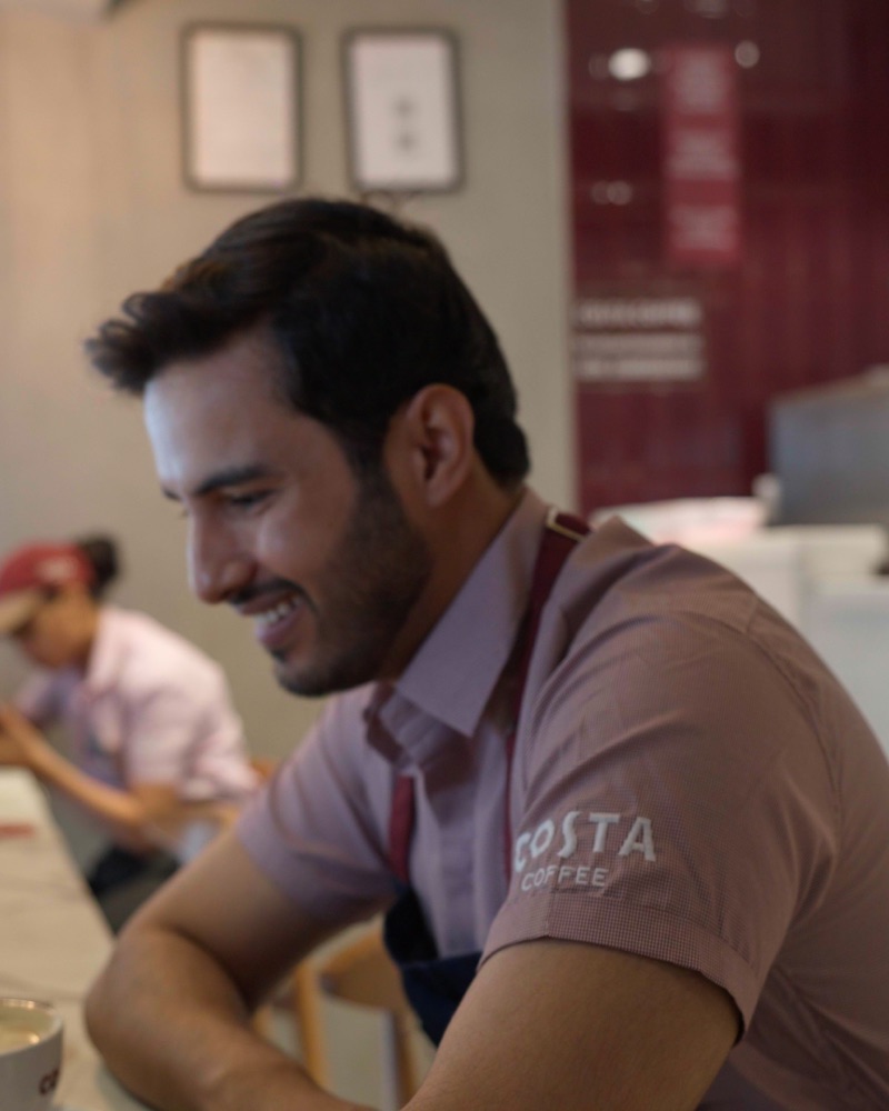 Smiling barista at a Costa Coffee counter